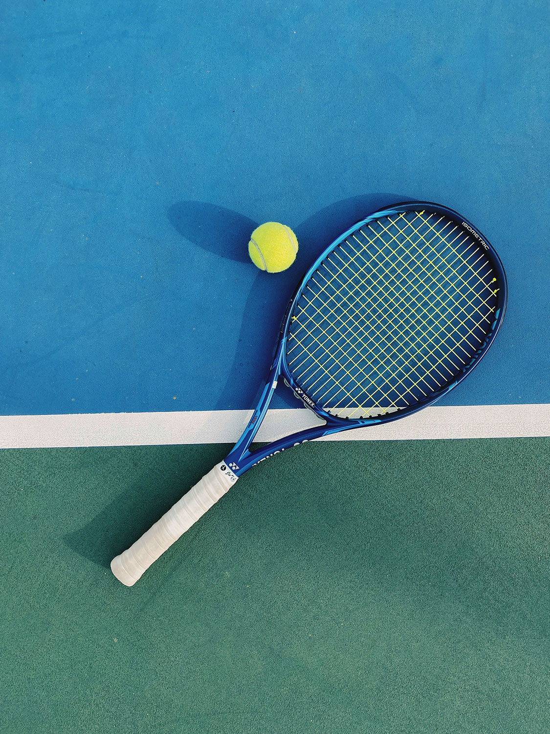 Tennis Tennis racket with a yellow ball on a blue tennis court near a white boundary line.